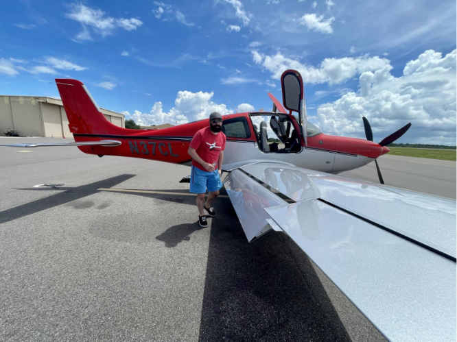 man next to red cirrus plane