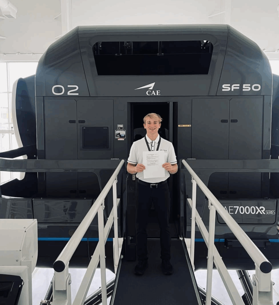 A student standing in front of an airplane simulator holding a certificate 
