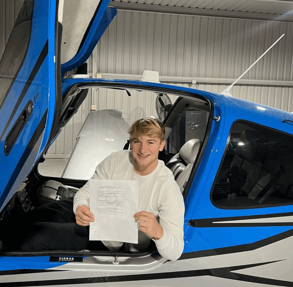 student holding a certificate while sitting in a a SR Series single engine plane